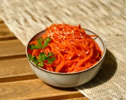 Carrot-Cha is a vibrant and flavorful salad made from finely shredded carrots, seasoned with a blend of spices, sesame seeds, and fresh herbs. Perfect as a zesty appetizer or side dish. Carrot-Cha salad in a bowl, featuring shredded spicy carrots garnished with sesame seeds and fresh parsley
